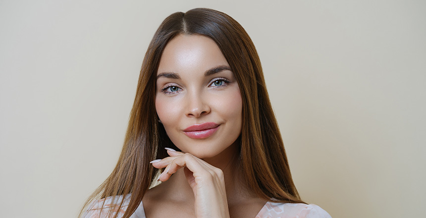 Portrait of beautiful dark haired young European woman touches jawline gently. She is considering jawline contouring.