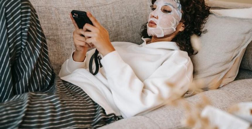 Woman lying on a couch with a facemask on -- she's researching alternative skincare treatments.